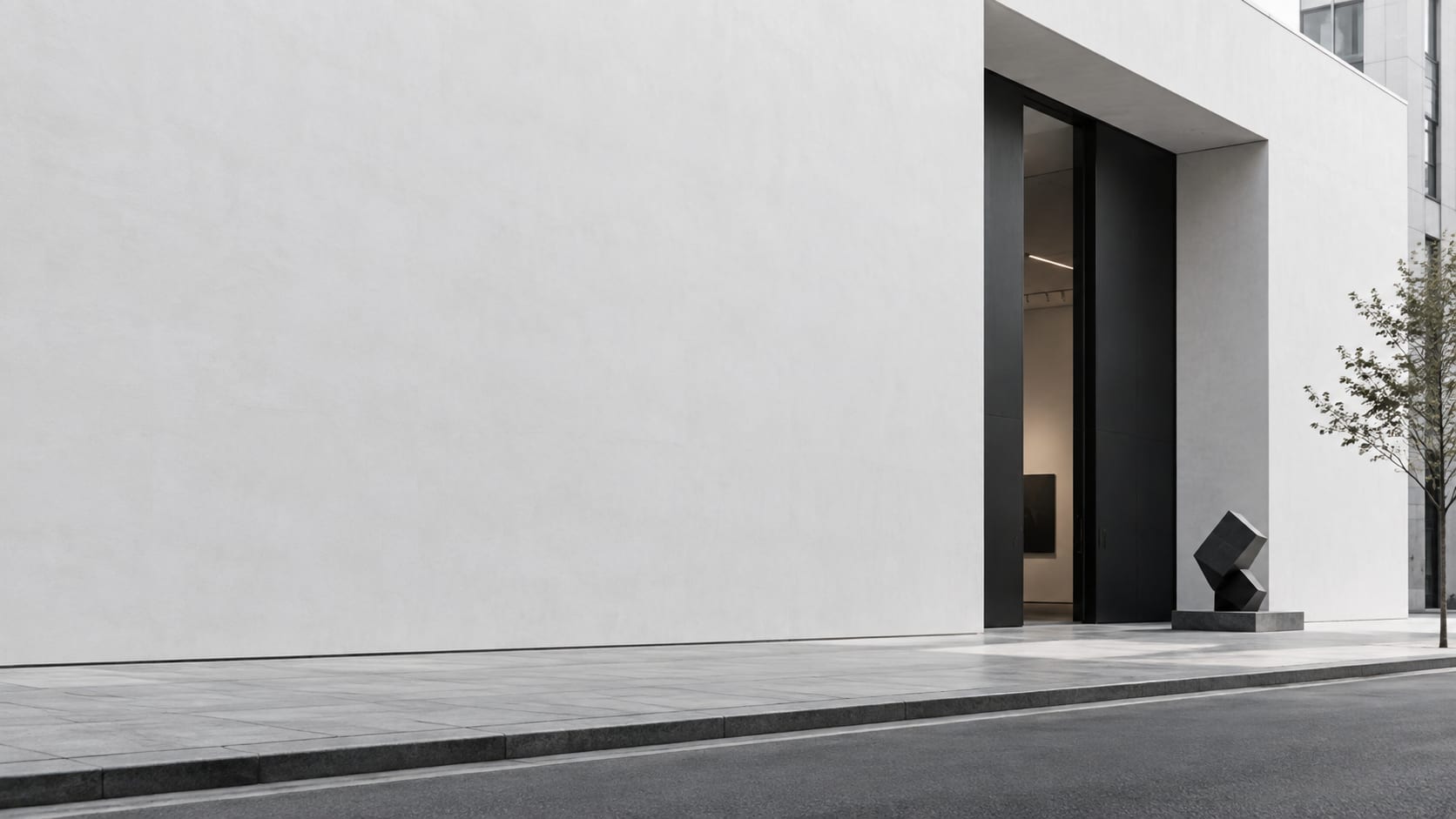 Fachada branca e lisa de uma galeria, com uma entrada alta e escura e uma escultura geométrica na calçada.
